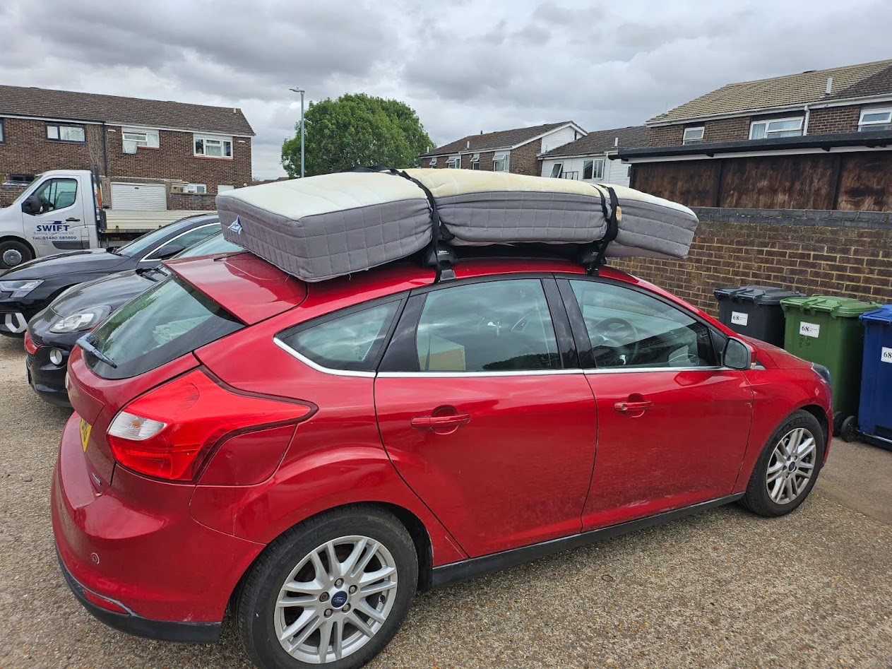 a red ford focus mk3 hatchback. It has a mattress strapped to the roof for some reason.